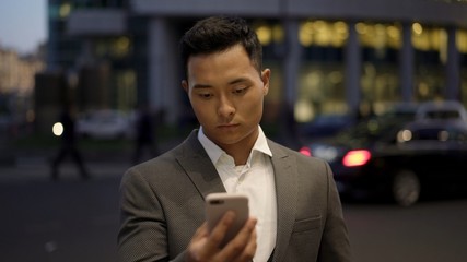 Front view of a young asian businessman, leading correspondence on the phone. Financial business area. Night time at business city.