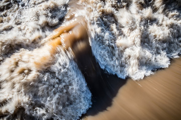Abstract of turbulent flood water rushing past bridge piling in Richmond, Virginia.