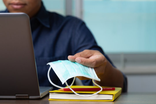 Male Employee And Heath Mask Reading Data From Computer Laptop While Working At Home To Win The Corona Virus, Covid-19.