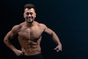 Fototapeta na wymiar male athlete shows body and muscles on dark wall background in gym, sexy guy bodybuilder, sports lifestyle, home sport.