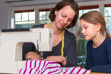 Mother teaches her 8 year old daughter how to sew a striped textiles with a sewing machine