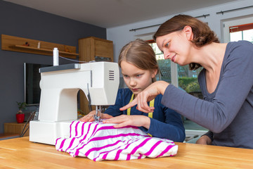 Mother teaches her 8 year old daughter how to sew a striped fabics with a sewing machine
