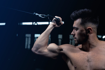 male athlete shows near the green simulator how to perform the exercise for the deltoid and biceps and triceps muscles in the gym, sexy guy bodybuilder, sports lifestyle, home sports.