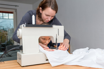 Mother teaches her 8 year old daughter how to sew a white fabics with a sewing machine