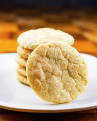 A stack of snickerdoodle cookies on a white plate.  Background blurry.  Focus on front facing cookie.