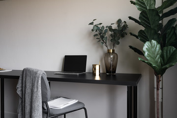 Bedroom working corner decorated with laptop, white candles and artificial plant in glass vase on black wood  working table with beige painted wall in the background /apartment interior / copy space