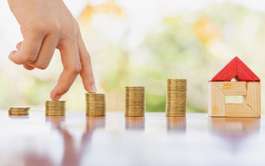hand walking on coin stack and house model resting on wooden desk