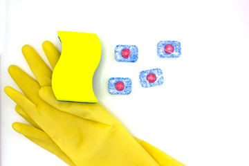 dishwashing products: sponge, dishwasher tablet, yellow gloves on white background. Top view, close up. Clean house and hand care concept