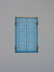 The window is covered with blue wooden shutters. The wall is light gray