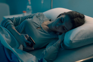 Sleepless patient lying in bed and chatting with her smartphone