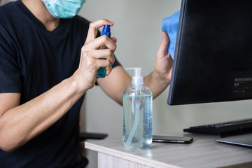 Fototapeta premium Man hand holding fabric and spraying alcohol 70% or disinfectant spray on laptop surface for prevention coronavirus (COVID-19), bacteria, virus and germ (select focus)