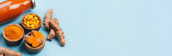 Turmeric in different states: fresh in bottle, pills, powder and cut plant on wooden tray, dry root in wooden bowl.