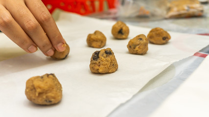 Close up view of woman preparing and putting raw mixes of cookies with chocolate chips on paper...