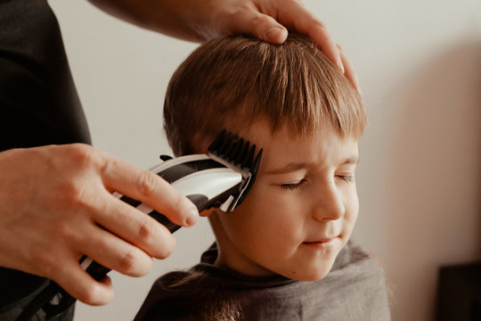 Kid Boy Getting A Haircut At Home. A Boy With A Dissatisfied Face