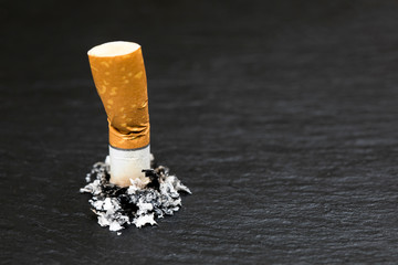 Stubbed cigarette butt stub with ash on black background.