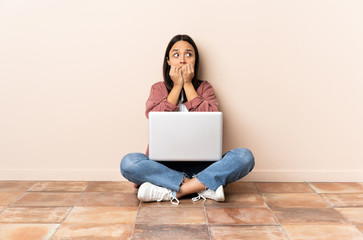 Young mixed race woman with a laptop sitting on the floor nervous and scared putting hands to mouth