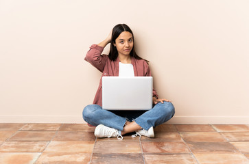 Young mixed race woman with a laptop sitting on the floor in back position and thinking