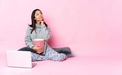 Young mixed race woman eating popcorn while watching a movie on the laptop looking up while smiling