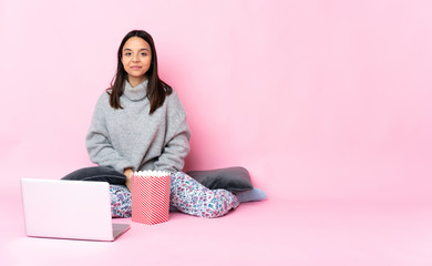 Young mixed race woman eating popcorn while watching a movie on the laptop in back position