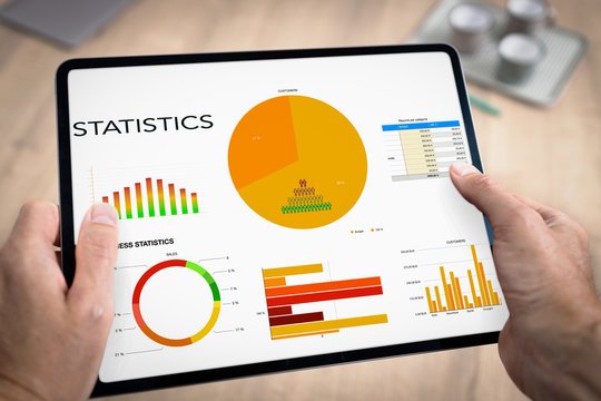 Tablette num&eacute;rique tenue en main par un homme au travail avec une pr&eacute;sentation de graphiques d'&eacute;volution de chiffre d'affaires et de statistiques