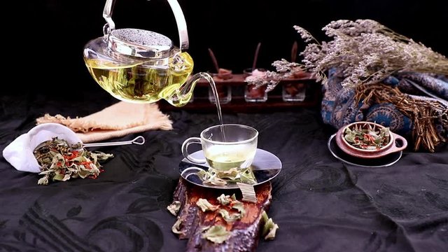 A Hot pandan leaf tea with indian marsh fleabane plant leaves and Safflower dried (Saffron substitute) is poured from the glass teapot into a glass with tea herbal and tea leave. Selective focus.