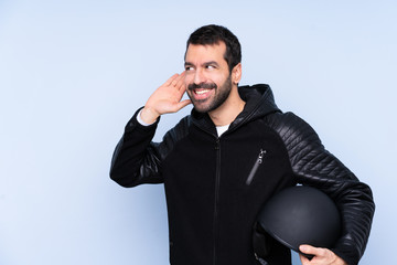 Man with a motorcycle helmet over isolated background listening to something by putting hand on the ear