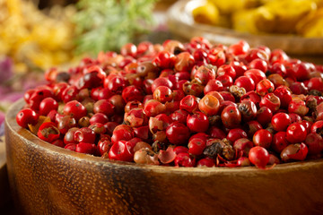red peppercorn seeds in wooden plate
