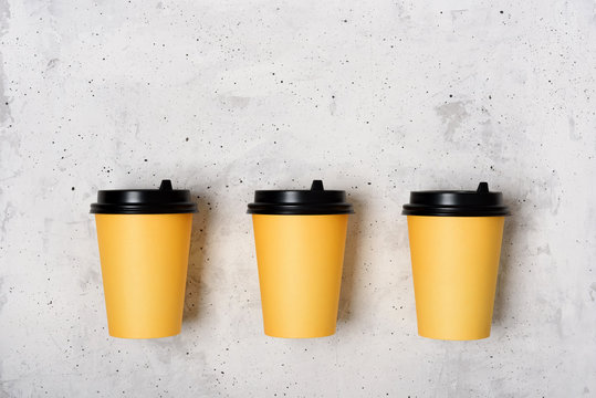 Three Yellow Paper Cups On A Light Gray Concrete Background. Place For Text From Above. Copy Space. Mockup. Minimalism Concept. Coffee To Go. Flatlay.