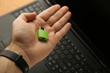 A hand holding a green padlock with a laptop in background. Cyber security concept image. 