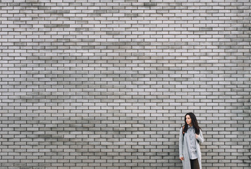 An young ukrainian woman with a backpack standing half a turn near the gray brick wall. The pensive look of a lonely girl is directed to his right. Stone texture with copy space.