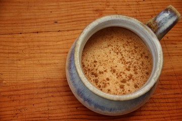 Chocolate milk with cinnamon in rustic light blue mug on wooden table. Closeup, macro, top view, flat lay, horizontal.