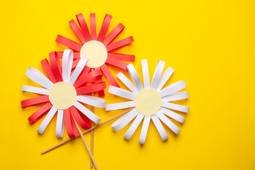 Three paper flowers on a yellow uniform background. DIY concept, children's art project.