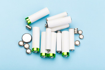 many new and used batteries of different shapes, AA, round batteries on a blue background.