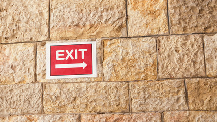 Red exit sign on sandstone textured wall 16:9 background