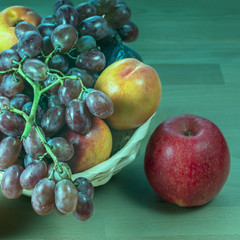 red grape berries and fresh fruits in a straw basket on a light wooden background