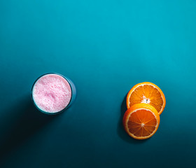 Dramatic illuminated gloomy smoothie and sliced orange view over blue oil background with minimal flat lay top view, copy space
