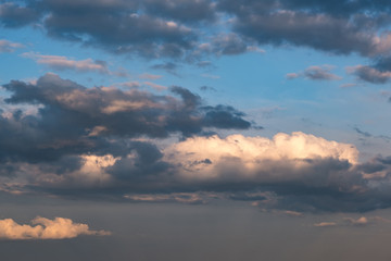 Blue sky background with evening fluffy curly rolling clouds. Good windy weather