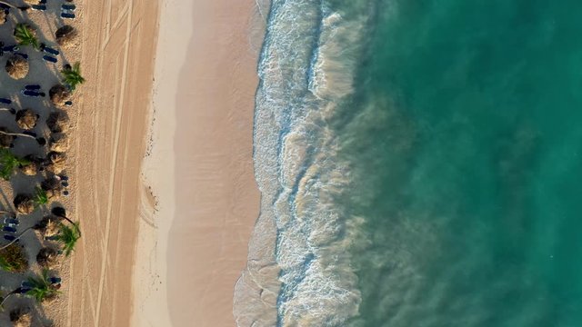 Drone flying back shot over luxury beach in Thailand. Aerial shot of ocean waves and sand beach with palm trees on the shore, texture of the water surface near the shore above
