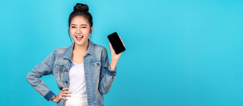 Banner Of Asian Woman Feeling Happiness, Blinks Eyes And Standing Hold Smartphone On Blue Background. Cute Asia Girl Smiling Wearing Casual Jeans Shirt And Connect Internet Shopping Online And Present