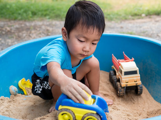 Asian child boy playing car toy in sandbox outdoor in rural nature background with smiling face....