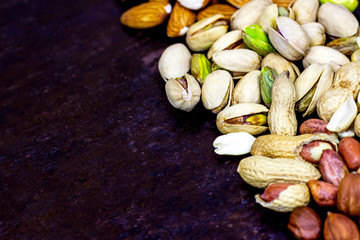 Top view of different nuts: almonds, pistachios, peanuts, hazelnuts on black metal background with copy space.