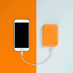 Smartphone and Powerbank on an orange and white background. Power bank charges the phone.