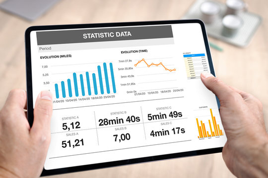 Tablette num&eacute;rique tenue en main par un homme au travail avec une pr&eacute;sentation d'affaires avec des graphiques de donn&eacute;es et des statistiques