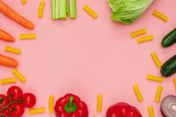 Flat lay from colored vegetables and pasta on a pink background. Space for text.