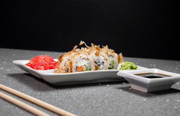 Rolls with tuna flakes and red fish on a white plate. Red Ginger White cup with soy sauce. Gray background. Chinese chopsticks