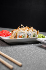 Rolls with tuna flakes and red fish on a white plate. Red Ginger White cup with soy sauce. Gray background. Chinese chopsticks