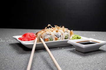 Rolls with tuna flakes and red fish on a white plate. Red Ginger White cup with soy sauce. Gray background. Chinese chopsticks