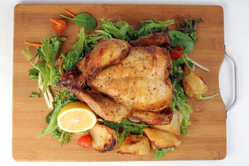 Whole roasted grilled chicken poultry bird with baked potato vegetable salad tomato lemon on wooden cutting board white background