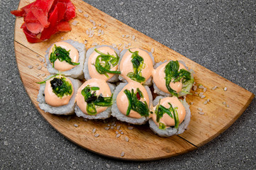 Rolls with algae on a wooden board. Red ginger. White cup with soy sauce. Gray background