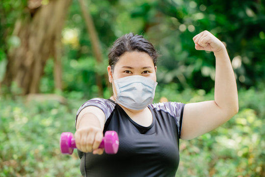 Healthy strong women exercise workout wear protective face mask for virus protection at public green park.